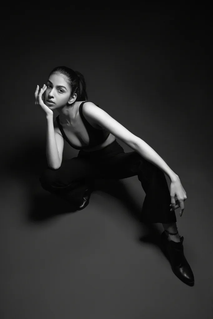 Black and white studio fashion photograph, model seated under a spotlight, photographed by Shreyak Singh